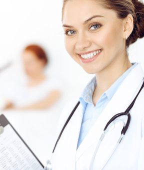 Cheerful smiling woman-doctor on the background his patient in the bed. Medicine concept.